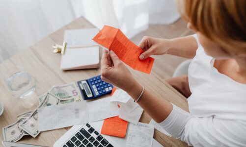 Kobieta siedząca przy biurku z laptopem, kalkulatorem i rachunkami w dłoniach.