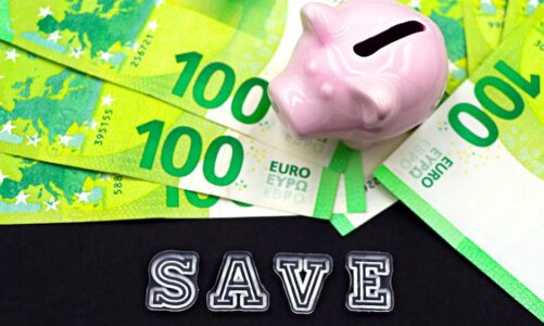 Różowa świnka skarbonka na tle rozłożonych banknotów studwudziestoeurowych z napisem SAVE.