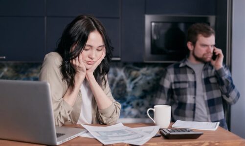 para w kuchni, kobieta siedzi przed laptopem i przegląda dokumenty, mężczyzna rozmawia przez telefon