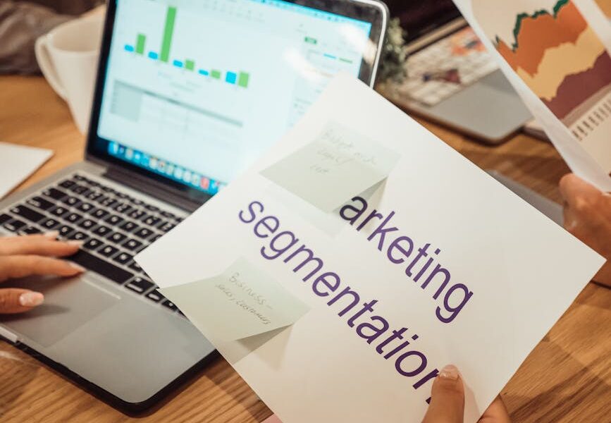kobieta siedząca przed komputerem z kartką z napisem "Marketing segmentation" w ręku
