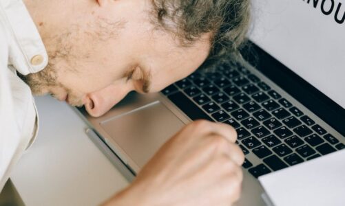 Mężczyzna śpiący z głową opartą na klawiaturze laptopa.